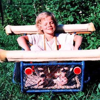 A child joyfully riding a homemade cart in grassy field.