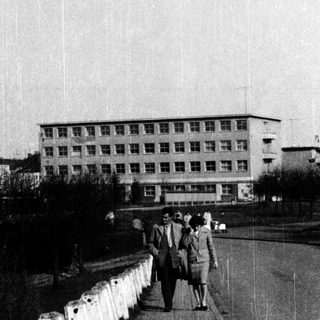People walking along a bridge near a large building.