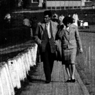 People walking along a bridge near a large building.