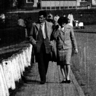 People walking along a bridge near a large building.