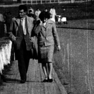 People walking along a bridge near a large building.