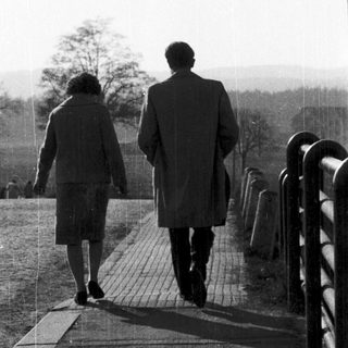 Two people walking together outdoors on a paved path.