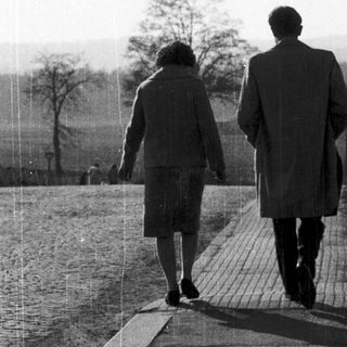 Two people walking together outdoors on a paved path.