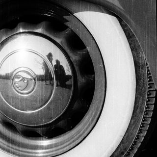 Reflection of person in shiny car hubcap.