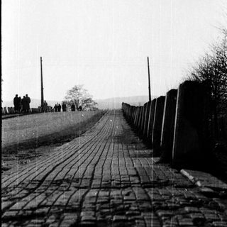 Historic roadway with cobblestone path and barbed-wire-topped barriers.