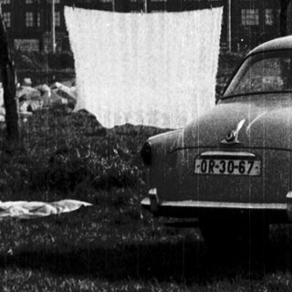 Man holding large white sheet near industrial building.