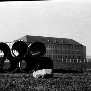 Large cylindrical concrete pipes in front of a building.