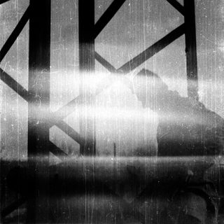 Silhouette of person standing under rain-soaked bridge.