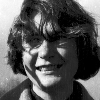 Smiling person with short, wavy hair outdoors.