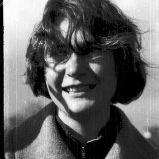 Smiling person with short, wavy hair outdoors.