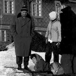 People in winter clothing near snow-covered building.