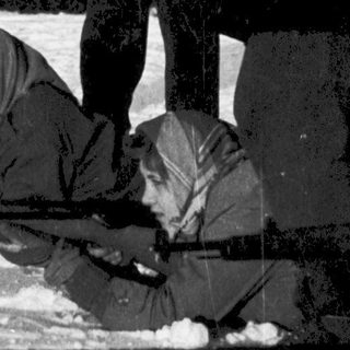 People in winter clothing near snow-covered building.