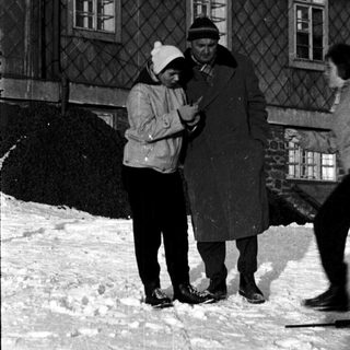 People skating on snow-covered ground near a building.