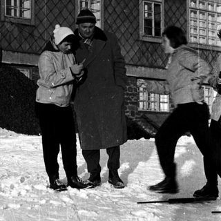 People skating on snow-covered ground near a building.
