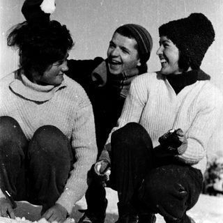 Three people laughing together in winter snow.