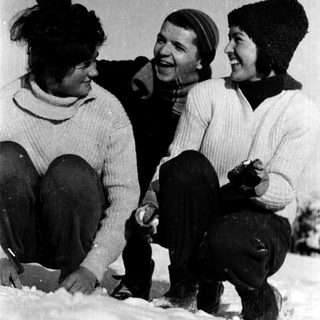 Three people laughing together in winter snow.