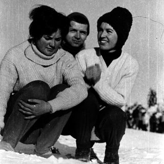 Three people posing happily in winter attire on snow.
