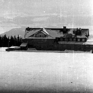 Vintage ski lodge with snow-covered slope and distant mountains.