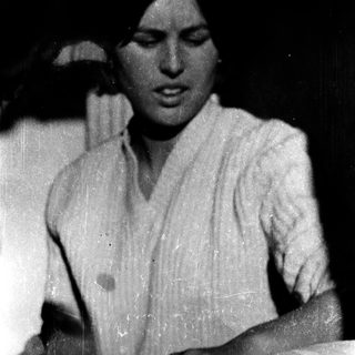 Young woman in vintage clothing, seated indoors.