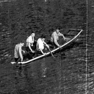 People rowing a small boat on a river near a path.