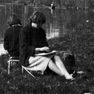 Two people sitting by flooded riverbank reading.