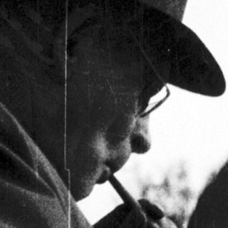 A man in outdoor attire smoking a pipe.