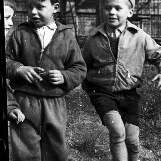 Two boys in vintage clothing pose outdoors.
