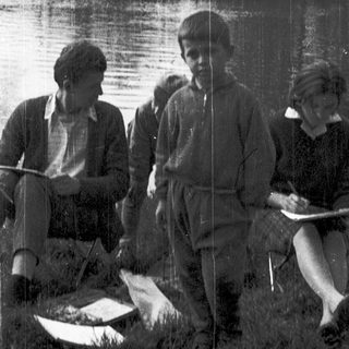 Three people by a lake, holding notebooks and a fish.