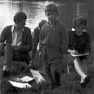 Three people by a lake, holding notebooks and a fish.