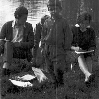 Three people by a lake, holding notebooks and a fish.