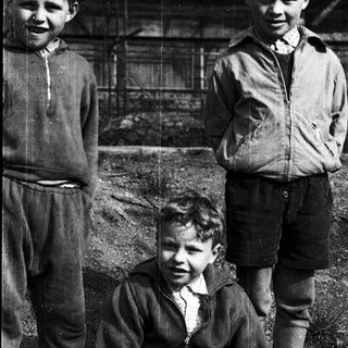 Three boys in early 20th-century clothing outdoors.