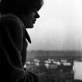 Person gazing thoughtfully outside rainy window.