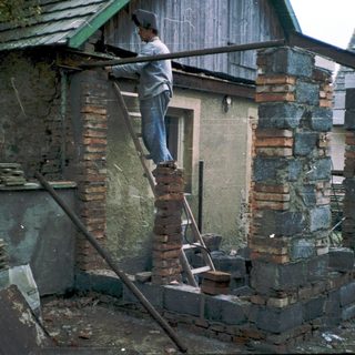 Person repairing damaged brick wall with ladder.