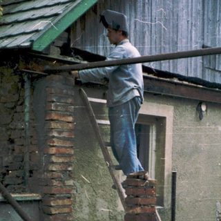 Person repairing damaged brick wall with ladder.