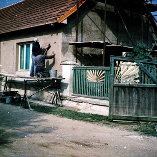 People painting and repairing a weathered house exterior.