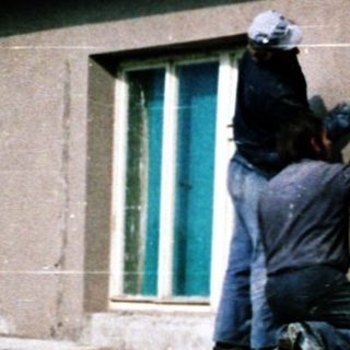 People painting and repairing a weathered house exterior.