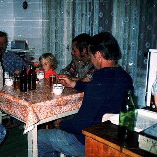 Family gathering around table with drinks and food.