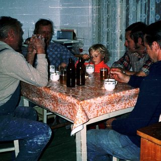 Family gathering around table with drinks and food.