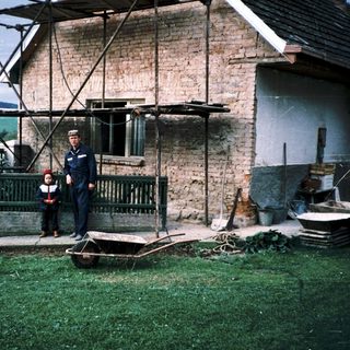 Two men in naval uniforms standing outside rustic brick house.
