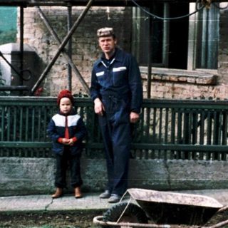 Two men in naval uniforms standing outside rustic brick house.
