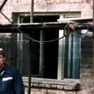 Two men in naval uniforms standing outside rustic brick house.
