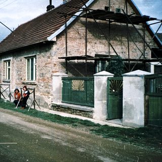 Rural house exterior with two people sitting, vintage sepia-toned photo.