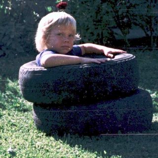 Child sitting on large tire outdoors.