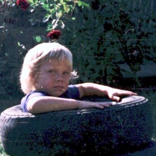 Child sitting on large tire outdoors.