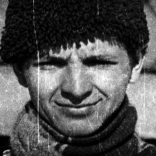Young man wearing winter hat and scarf outdoors.