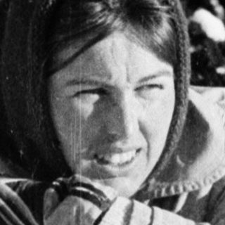 Woman skiing in snowy forest, holding poles.