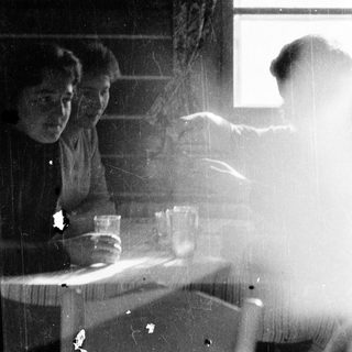 Two people sitting indoors near a window, another person standing outside in rain.