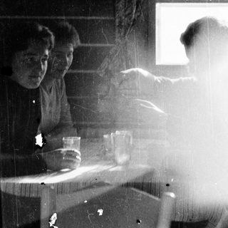 Two people sitting indoors near a window, another person standing outside in rain.