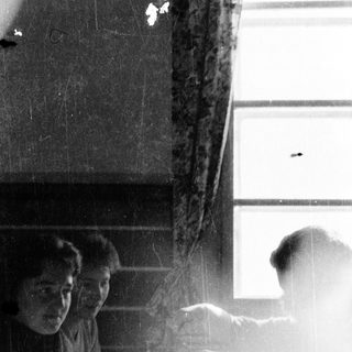Two people sitting indoors near a window, another person standing outside in rain.
