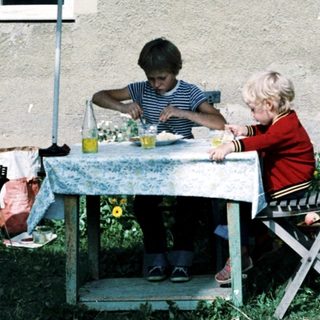 Two children eating outdoors under umbrella.